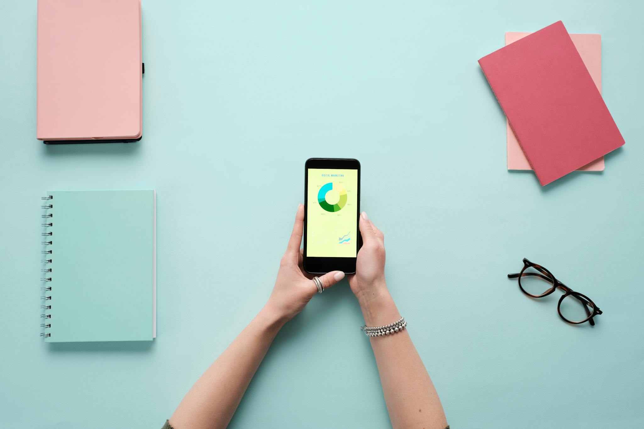 Overhead view of smartphone displaying business analytics on a vibrant blue background with stationery items.